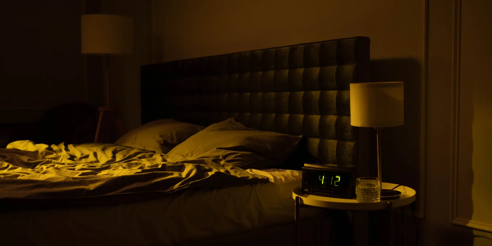 Chambre à coucher tamisée la nuit, lit défait sous une lumière chaude